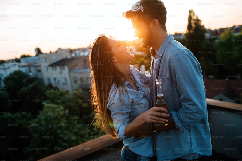 Casal flertando enquanto toma uma bebida no terraço ao pôr do sol