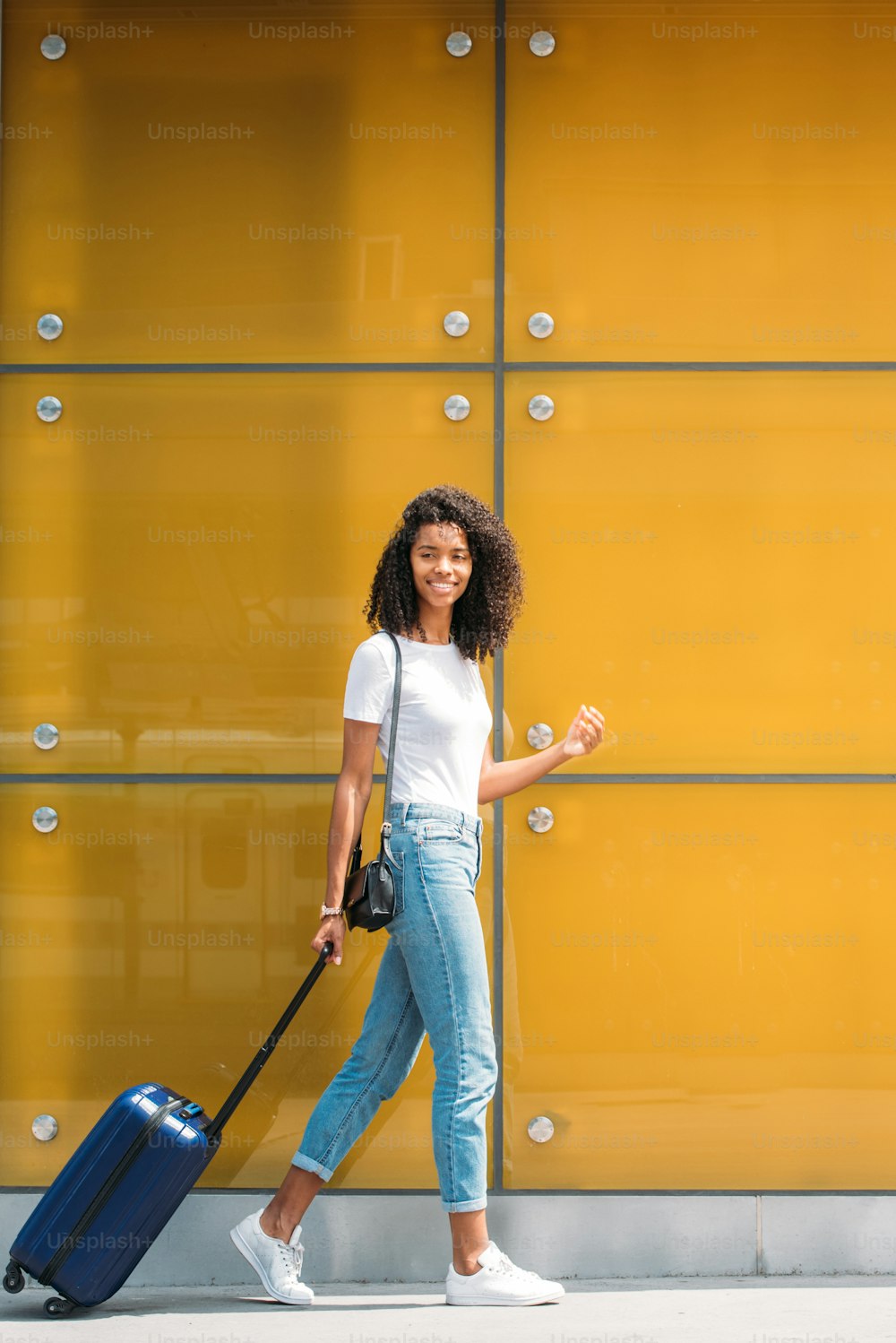Woman walking and pushing a suitcase in a yellow glass background