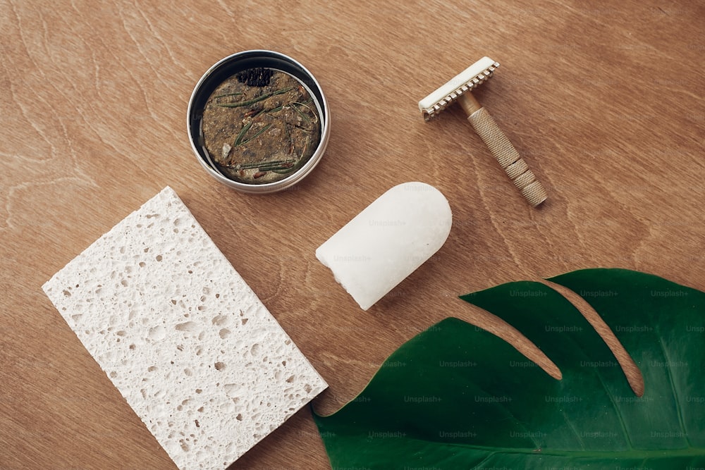 Natural soap, solid shampoo in metal tin, reusable razor, crystal eco deodorant, sponge on wooden background with green monstera leaf. Plastic free beauty essentials. Zero waste concept, flat lay