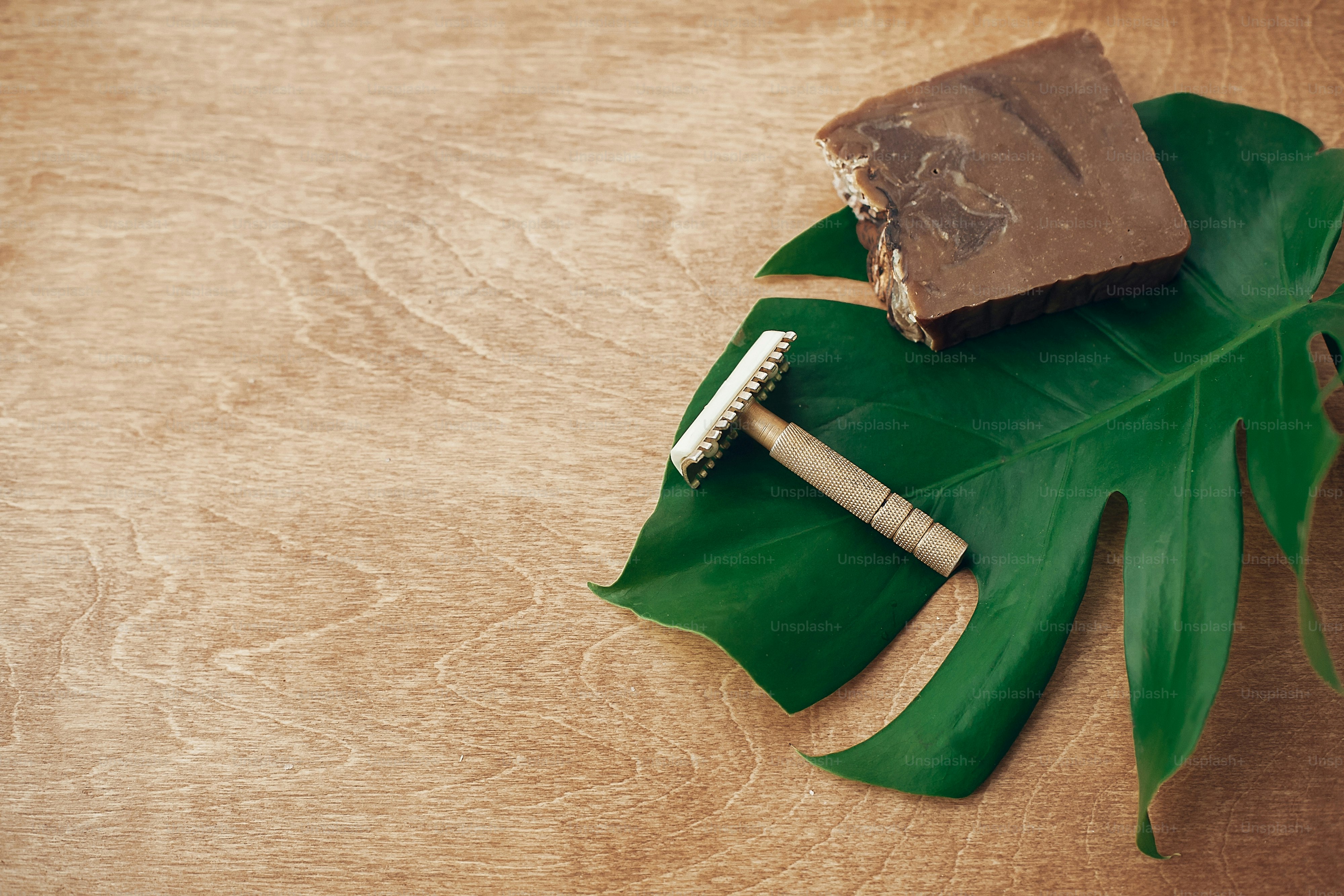 Natural eco soap and reusable metal razor on wooden background with green monstera leaf. Plastic free beauty essentials. Zero waste concept, copy space. Sustain
