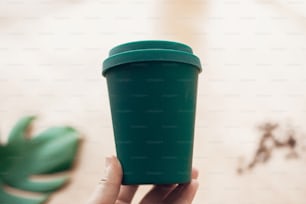 竹繊維のコーヒーカップ、廃棄物ゼロのコンセプト。使い捨てプラスチックの禁止。カップにコーヒーを入れます。サステナブルなライフスタイル。木製の背景にエココーヒーカップを持つ手。