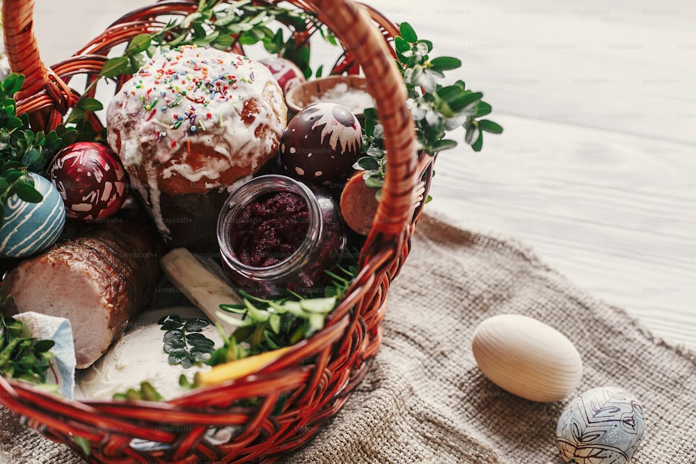 stylish easter basket with food. horseradish, beetroot, ham, butter, buxus, sausage and painted eggs in wicker  basket. happy easter. space for text