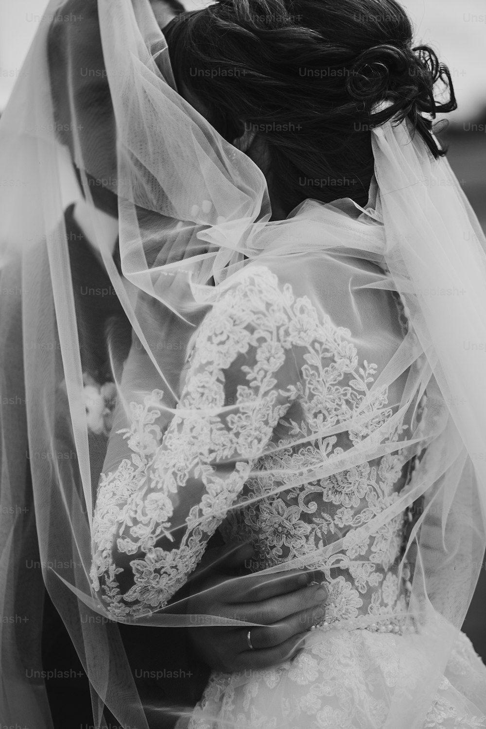 Stilvolle glückliche Braut und Bräutigam, die sich unter Schleier umarmen und umarmen, in der Nähe von Retro-Auto. Luxus-Hochzeitspaar Brautpaar, sinnlicher romantischer Moment. Platz für Text. Schwarz-Weiß-Foto