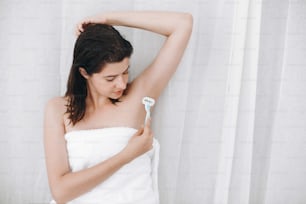 Junge Frau rasiert Achselhöhlen mit Plastikrasierer Nahaufnahme im heimischen Badezimmer. Hautpflege. Haarentfernungskonzept. Speicherplatz kopieren. Hand halten Plastikrasierer und glatte Achselhöhle rasieren.