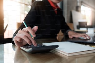 Close up of businessman or accountant hand holding pencil working on calculator to calculate financial data report, accountancy document and laptop computer at office, business concept