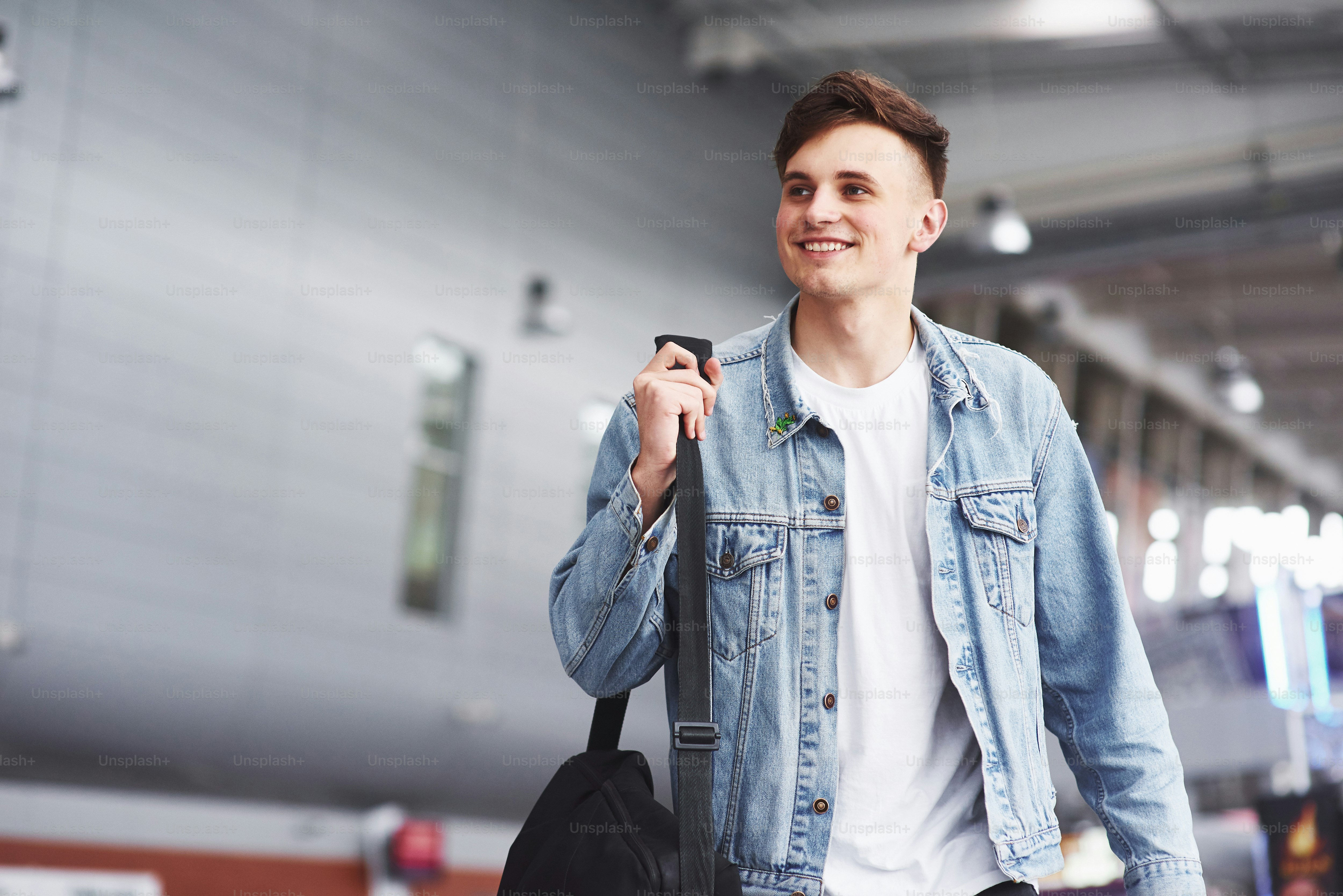 Joven guapo con una bolsa al hombro a toda prisa hacia el aeropuerto.