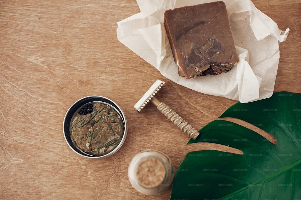 Zero waste concept, flat lay. Natural soap, solid shampoo in metal tin, reusable razor, ubtan on wooden background with green monstera leaf. Plastic free beauty essentials. Ban plastic