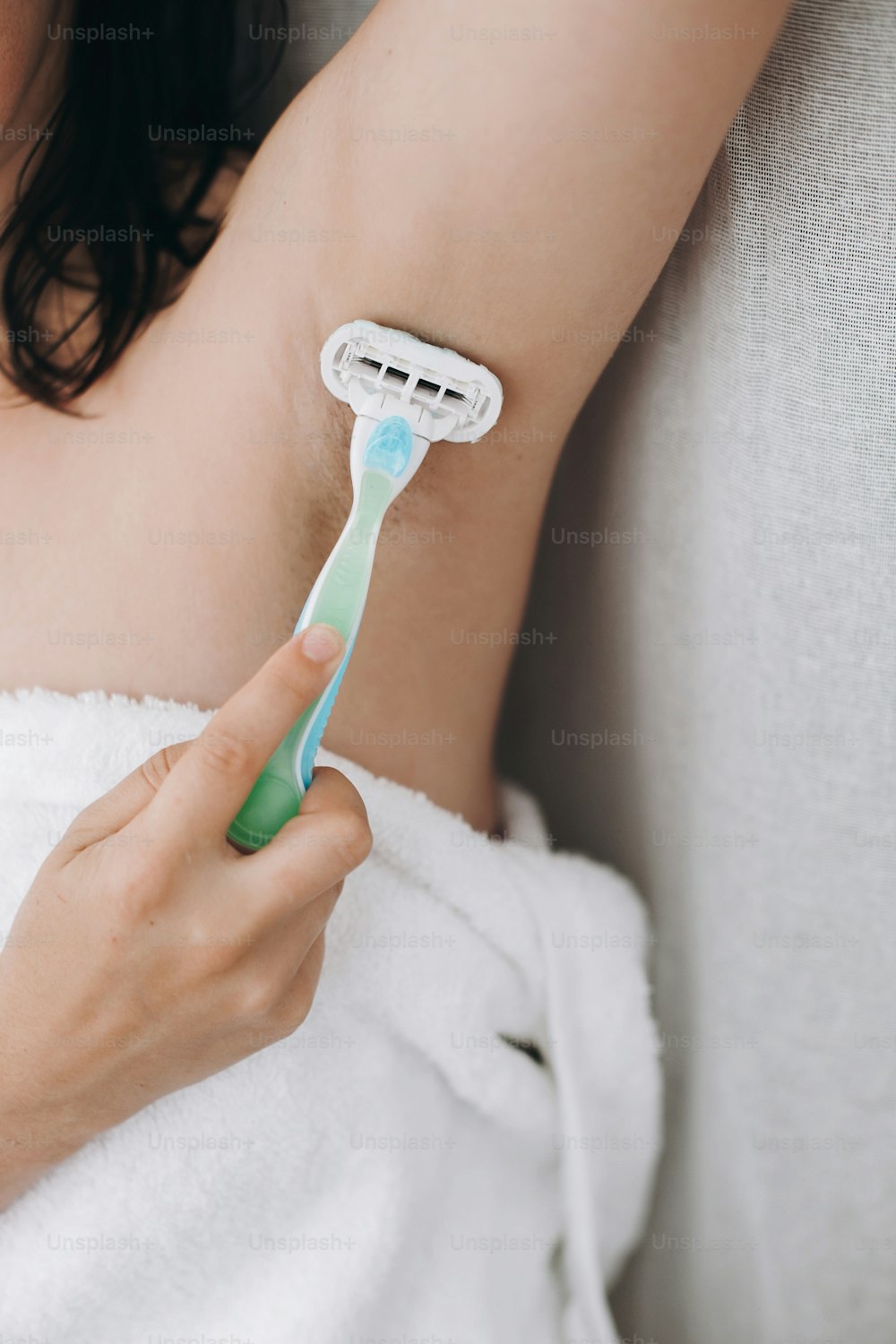 Hand holding plastic razor and shaving hairy armpit. Young woman shaving armpits with plastic razor closeup in home bathroom. Skin care. Hair Removal concept. Copy space