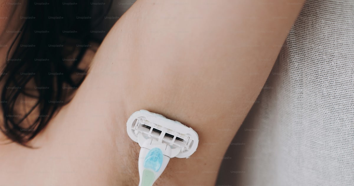 Hand holding plastic razor and shaving hairy armpit. Young woman ...