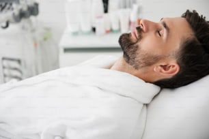 Close up of relaxed man in white bathrobe lying with his eyes closed and smiling