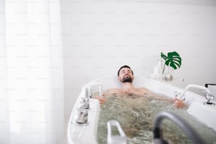 Bel homme barbu joyeux se relaxant dans une baignoire d’hydromassage et souriant tout en en profitant