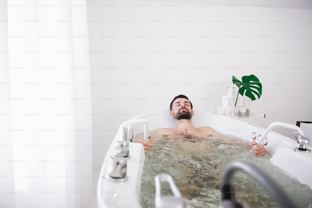Cheerful handsome bearded man relaxing in hydro massage bathtub and smiling while enjoying it