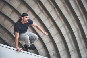 young man doing parkour jump in urban space in the city sunny spring summer day