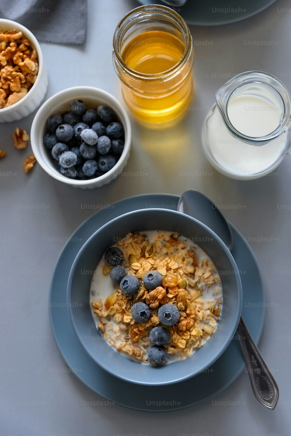 Tazón de granola (gachas de avena) con arándanos, miel y leche sobre mesa gris. Plano tendido. Enfoque selectivo. Comida vegetariana saludable
