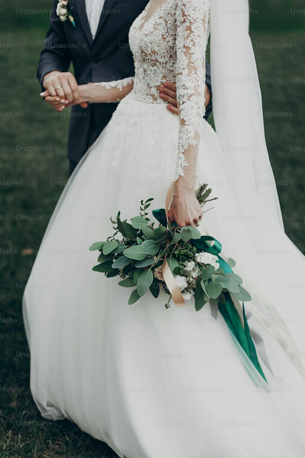 Stilvolle glückliche Braut und Bräutigam, die im Hof spazieren gehen und bei der Hochzeitszeremonie Händchen halten. Romantischer Moment, Platz für Text. Luxushochzeit Brautpaar, Boho-Blumenstrauß und Kleid Nahaufnahme