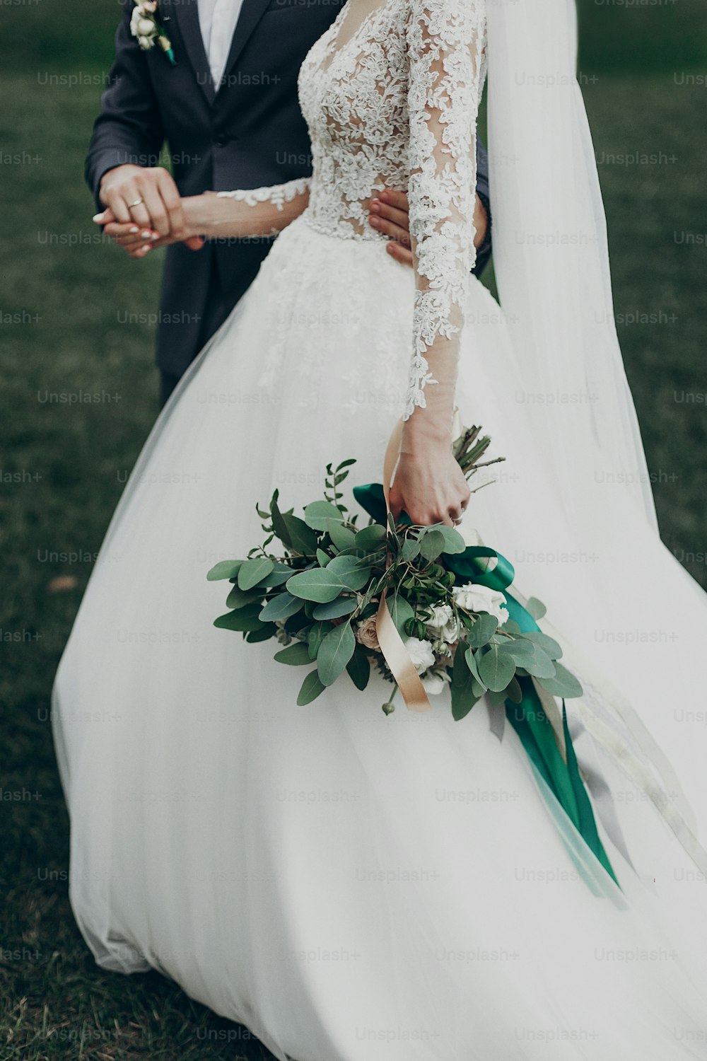 stylish happy bride and groom walking in yard and holding hands at wedding ceremony. romantic moment, space for text. luxury wedding newlyweds couple, boho bouquet and gown close-up
