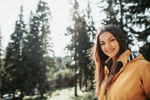 Positive emotions. Close up portrait of beautiful girl in yellow jacket posing in forest on blurred background. She is looking at camera with smile