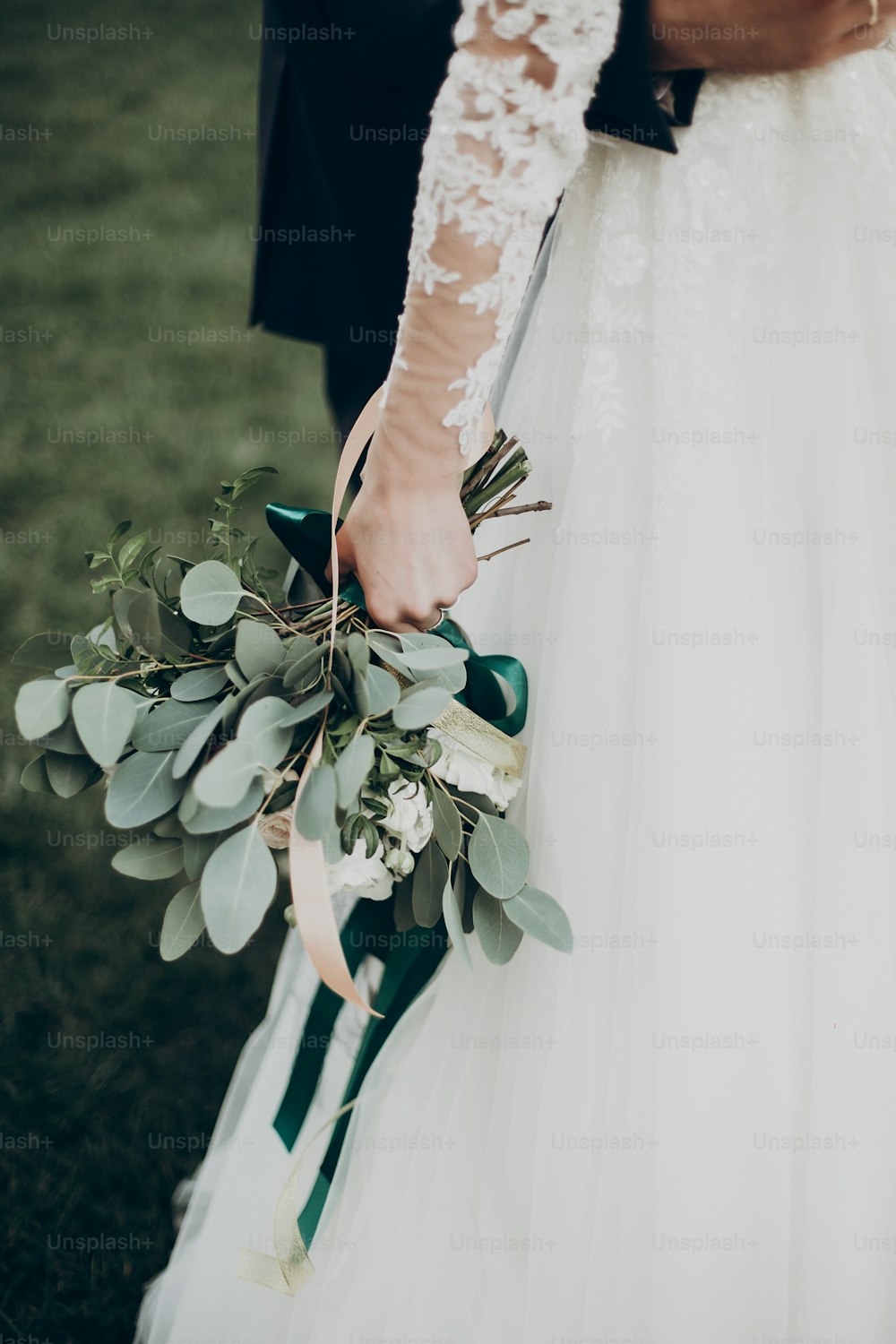 세련되고 행복한 신부는 보헤미안 소박한 녹색 꽃다발을 들고 공원에서 신랑과 포옹합니다. 낭만적 인 순간, 텍스트를위한 공간. 럭셔리 웨딩 신혼 부부, 뒷모습