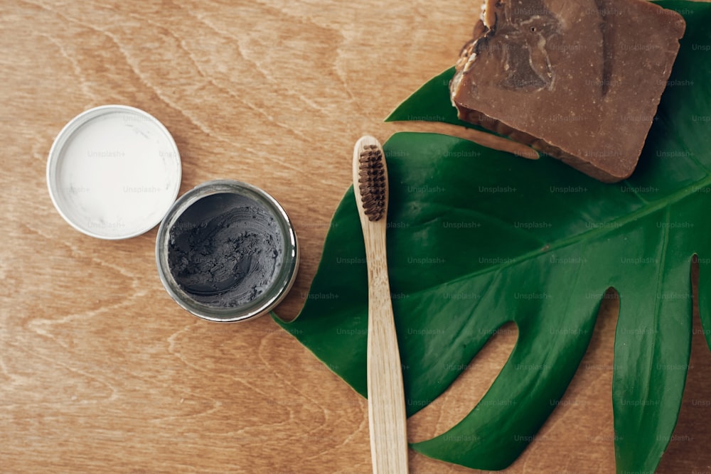 Natural toothpaste activated charcoal and bamboo toothbrush on wooden background with green monstera leaf. Plastic free beauty essentials, teeth care. Zero waste concept. Sustainable lifestyle
