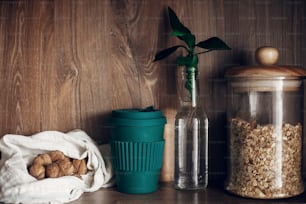 Bulk store shopping. Glass jar with cereals, textile reusable bags with nuts, reusable coffee cup and bamboo leaves on wooden shelf. Zero waste concept, sustainable lifestyle. Ban  plastic