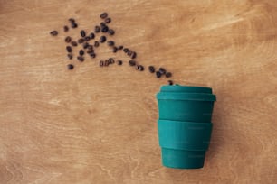 Zero waste concept, flat lay. Stylish reusable eco coffee cup on wooden background with roasted coffee beans. Ban single use plastic. Sustainable lifestyle. Natural bamboo cup