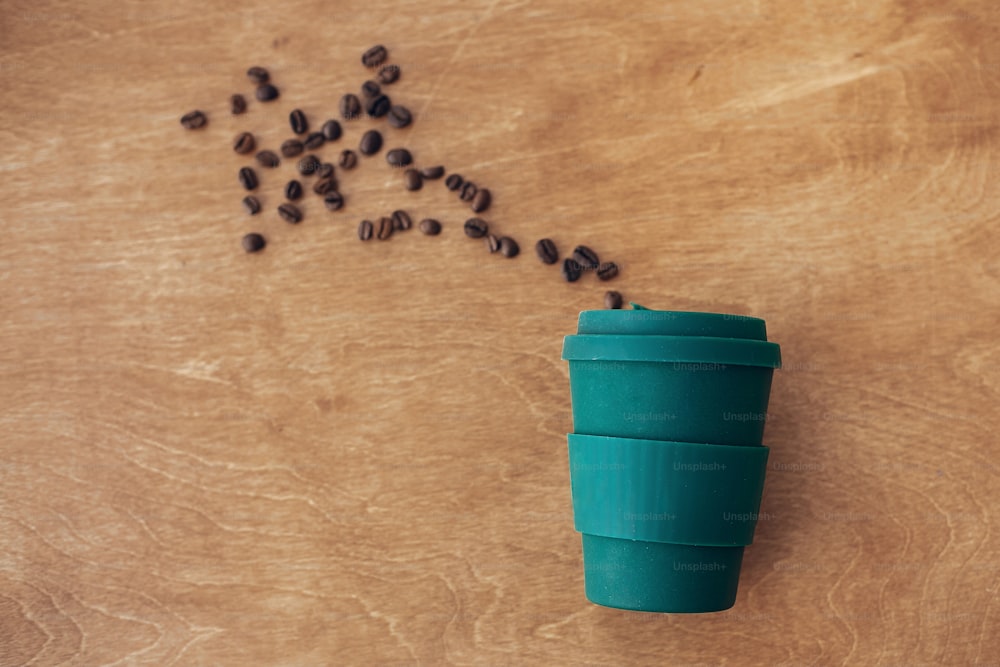 Concept zéro déchet, mise à plat. Tasse à café écologique réutilisable élégante sur fond en bois avec grains de café torréfiés. Interdire le plastique à usage unique. Mode de vie durable. Tasse en bambou naturel