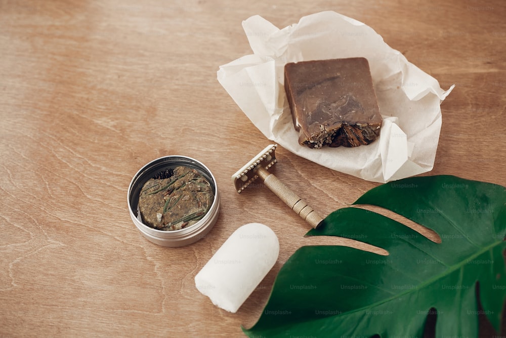 Natural soap, solid shampoo in metal tin, reusable razor, crystal eco deodorant on wooden background with green monstera leaf. Plastic free beauty essentials. Zero waste concept. Sustainable lifestyle