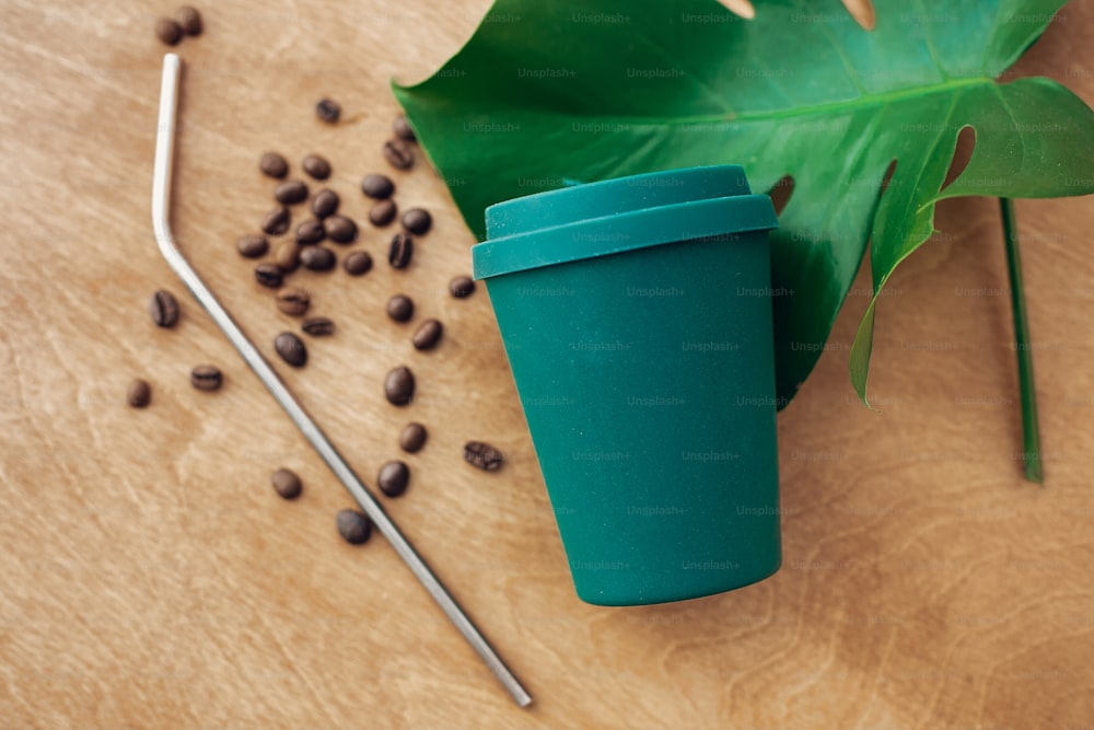 Zero waste concept. Stylish reusable eco coffee cup and metallic steel straws on wooden background with green monstera leaf. Ban single use plastic. Sustainable lifestyle