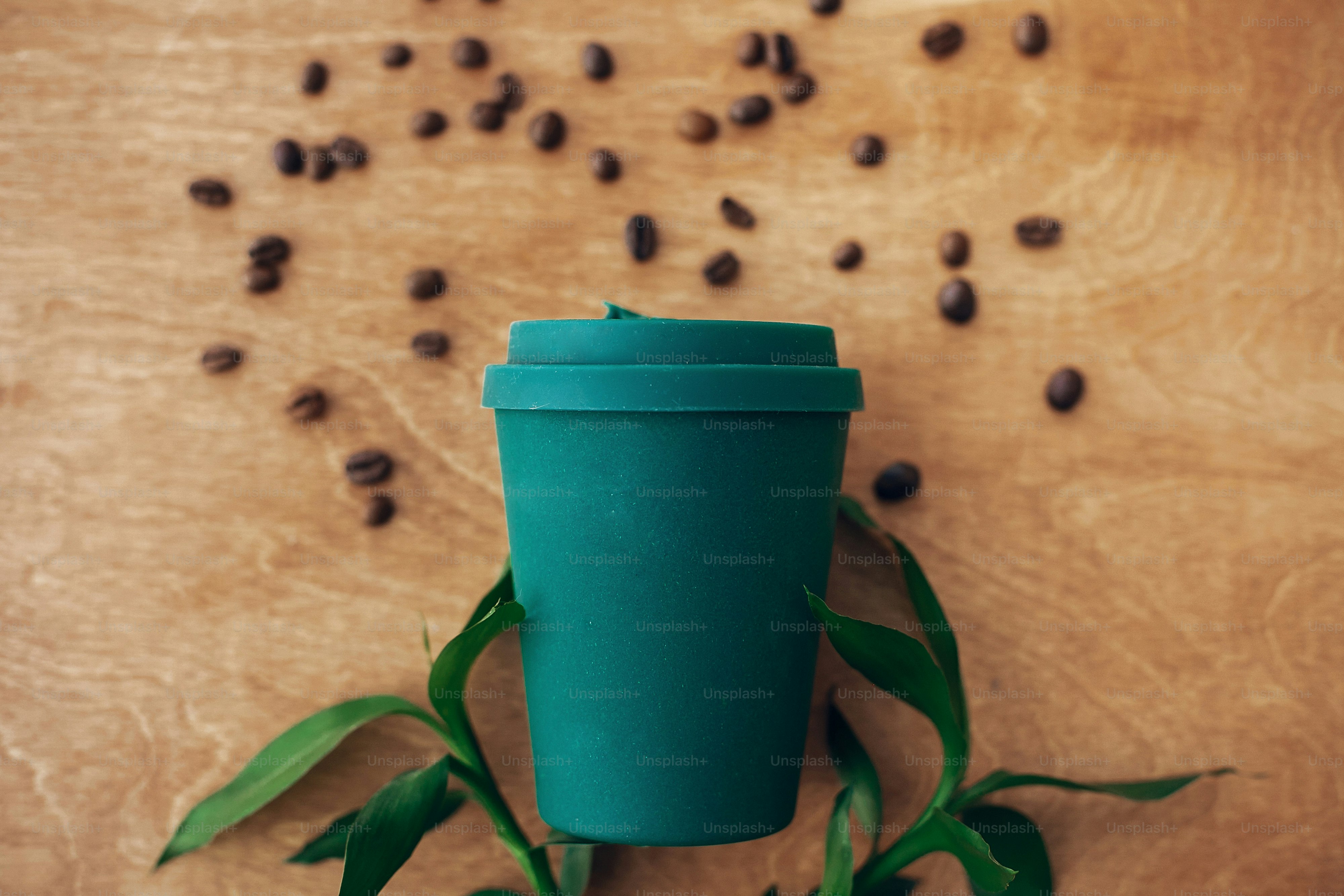 Zero-Waste-Konzept, flache Verlegung. Stilvolle wiederverwendbare Öko-Kaffeetasse auf Holzhintergrund mit Kaffeebohnen und grünen Bambusblättern. Verbot von Einwegplastik. Nachhaltiger Lebensstil. Natürlicher Bambusbecher