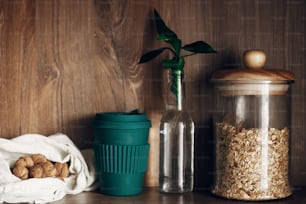 Glass jar with cereals, reusable shopping bag with nuts, reusable coffee cup and bamboo leaves on wooden shelf. Zero waste concept, bulk store shopping. Sustainable lifestyle. Ban plastic