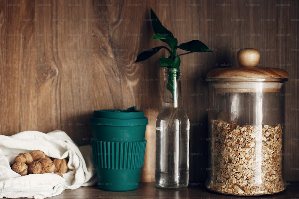 Glass jar with cereals, reusable shopping bag with nuts, reusable coffee cup and bamboo leaves on wooden shelf. Zero waste concept, bulk store shopping. Sustainable lifestyle. Ban plastic