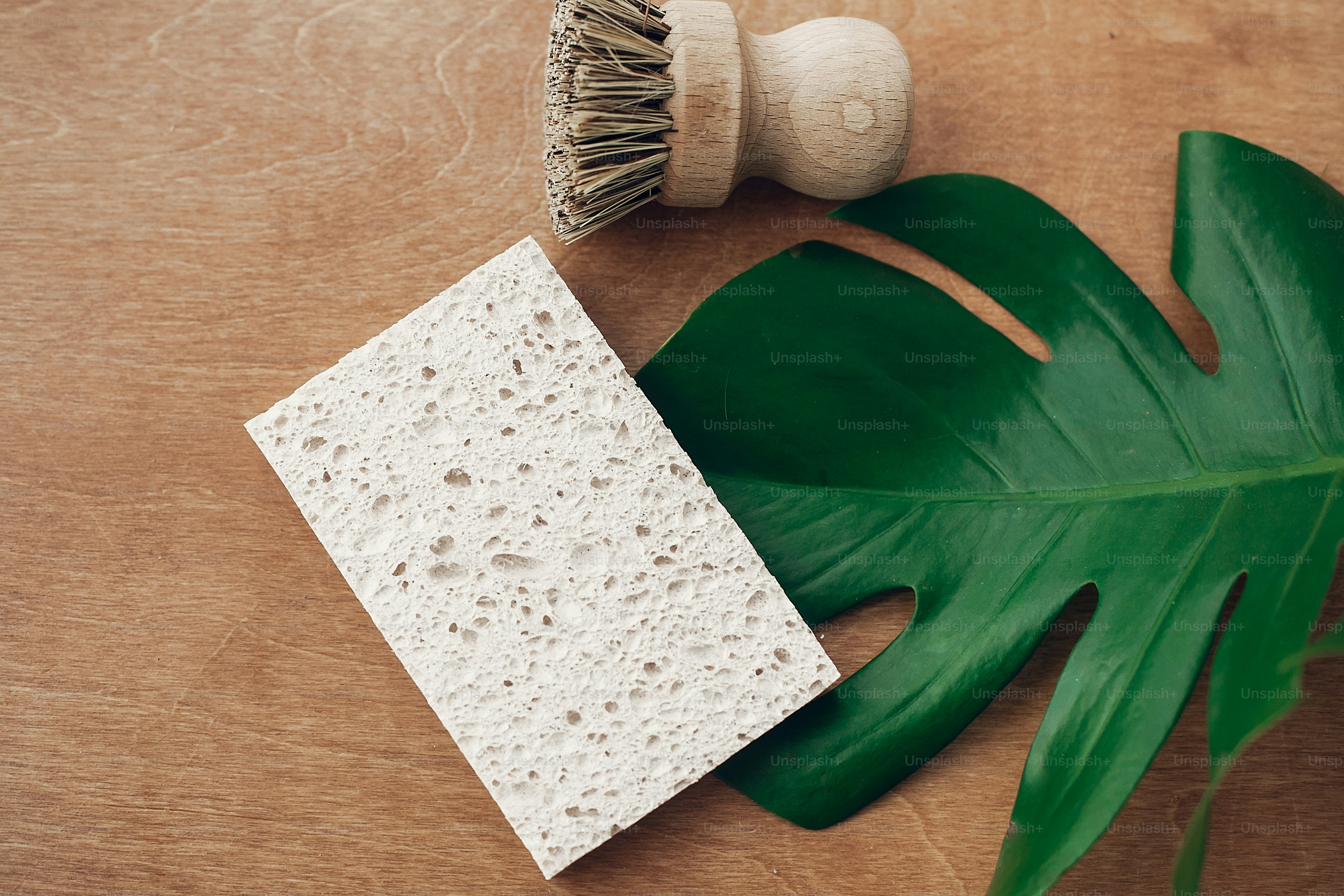 Zero waste concept, flat lay. Reusable natural cellulose sponge and eco wooden brush on wooden background with green monstera leaf. Ban single use plastic. Sustainable lifestyle.