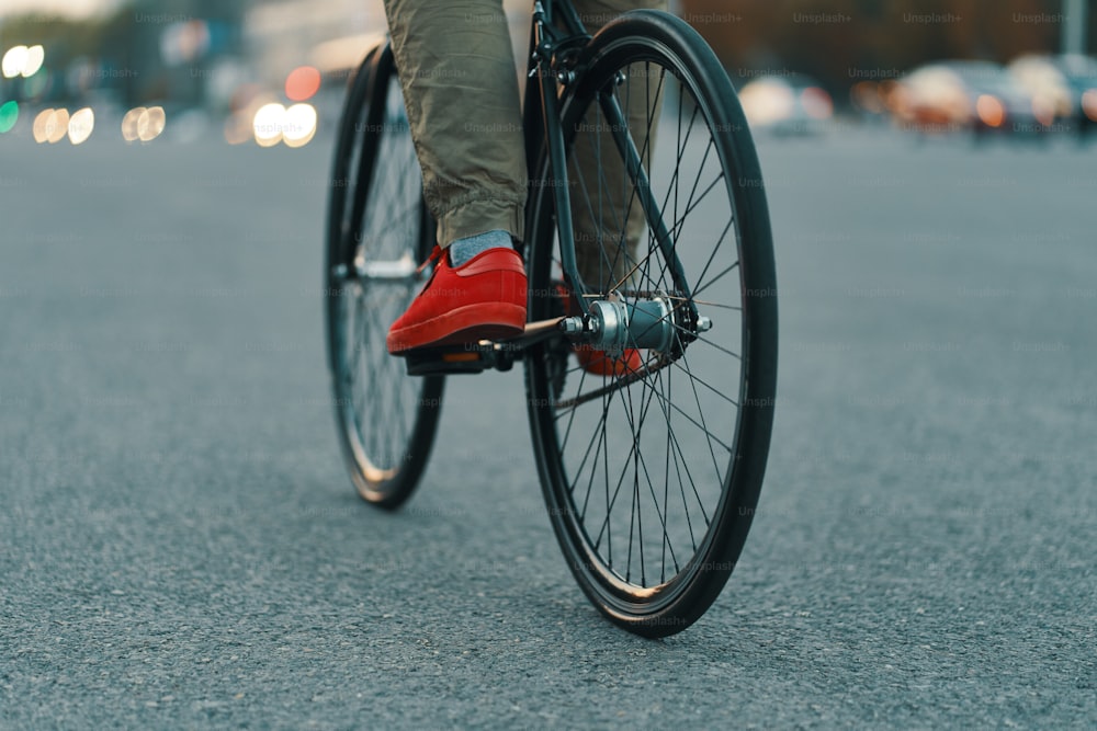 赤いスニーカーと快適なズボンを身に着けて、街の灰色の道路でクラシックバイクに乗っているカジュアルな男性の足の接写。コピースペース