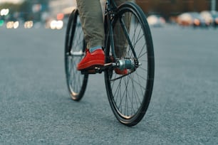 Primer plano de piernas de hombre casual montando una bicicleta clásica en la carretera gris de la ciudad con zapatillas rojas y pantalones cómodos. Espacio de copia