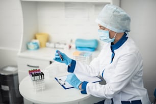 Investigación profesional de laboratorio en el sistema sanitario. Asistente femenina de la instalación mirando el tubo de ensayo de sangre en la oficina del laboratorio