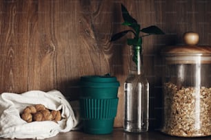 Bulk store shopping. Glass jar with cereals, textile reusable bags with nuts, reusable coffee cup and bamboo leaves on wooden shelf. Zero waste concept, sustainable lifestyle. Ban  plastic