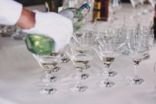 Garçom derramando martini em copos de cristal na festa de mesa na recepção do casamento. Martini fila bebidas no bar de bebidas alcoólicas. Festa de Natal e Ano Novo. Celebrações e conceito de festa.