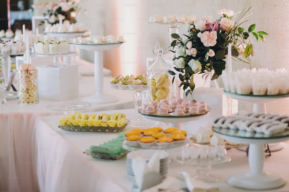 Délicieux éclairs, macarons, cupcakes, desserts et bonbons à table lors de la réception de mariage. Bar à bonbons élégant blanc et rose. Fête de Noël et du Nouvel An. Célébrations et fête