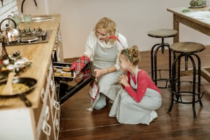 Preparing cookies. Smiling beaming daughter with deer ears showing her job to proud blonde mother