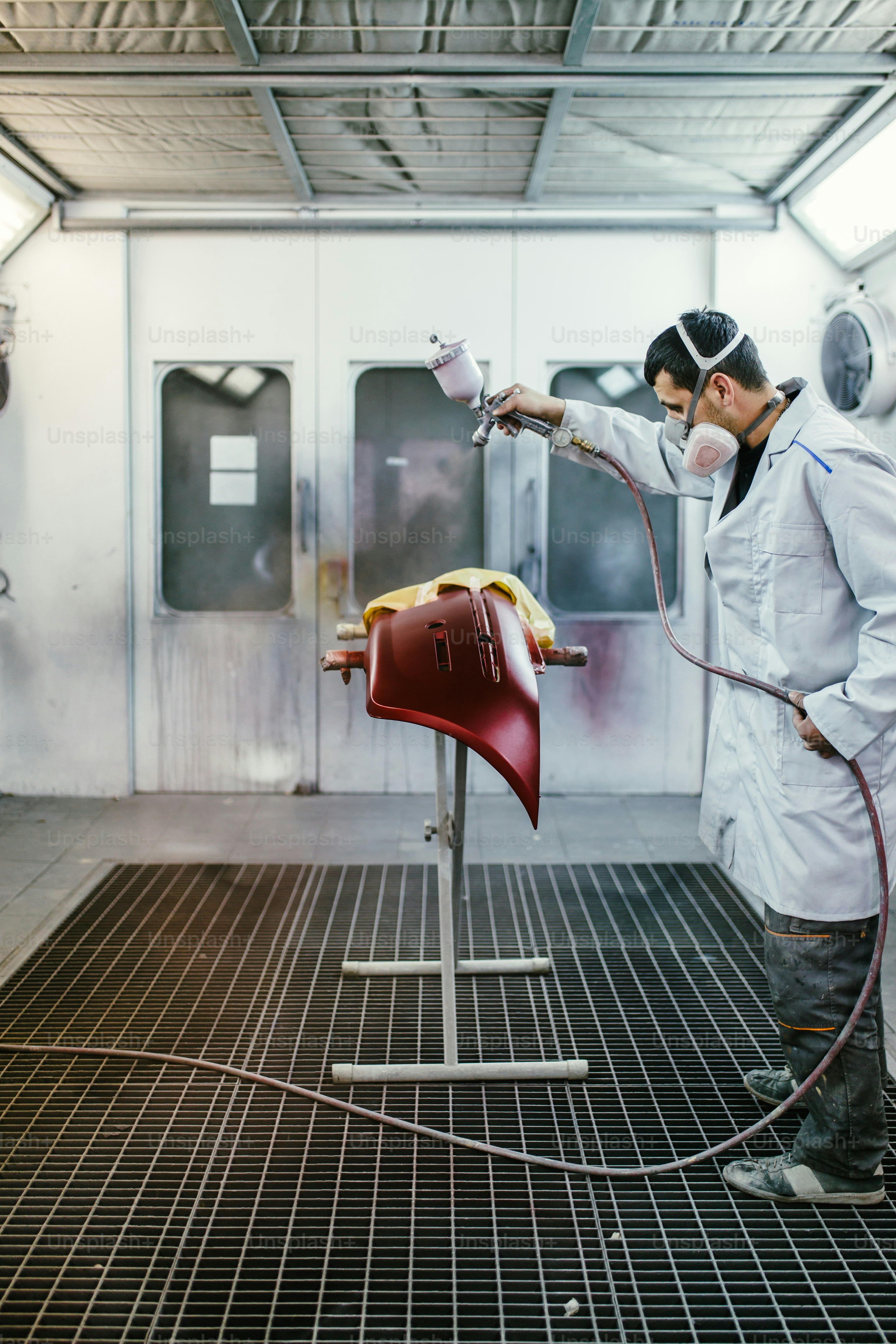 Man with protective clothes and mask painting car parts using spray