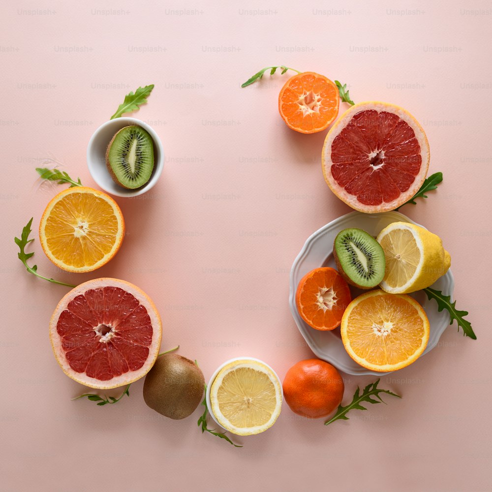 Marco de frutas tropicales de naranja, limón, mandarina y kiwi sobre fondo de papel rosa. Concepto de comida saludable. Tendido plano. Vista superior