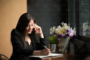 Empresaria asiática que llama por teléfono móvil y toma notas en la oficina