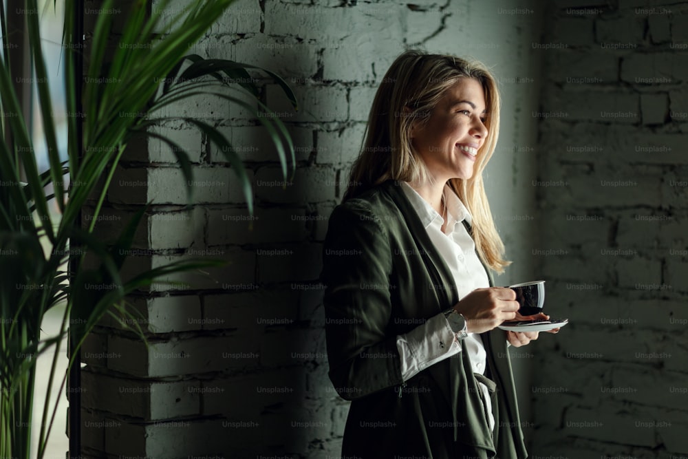 Junge lächelnde Frau mit Tasse Kaffee steht an der Wand und träumt.