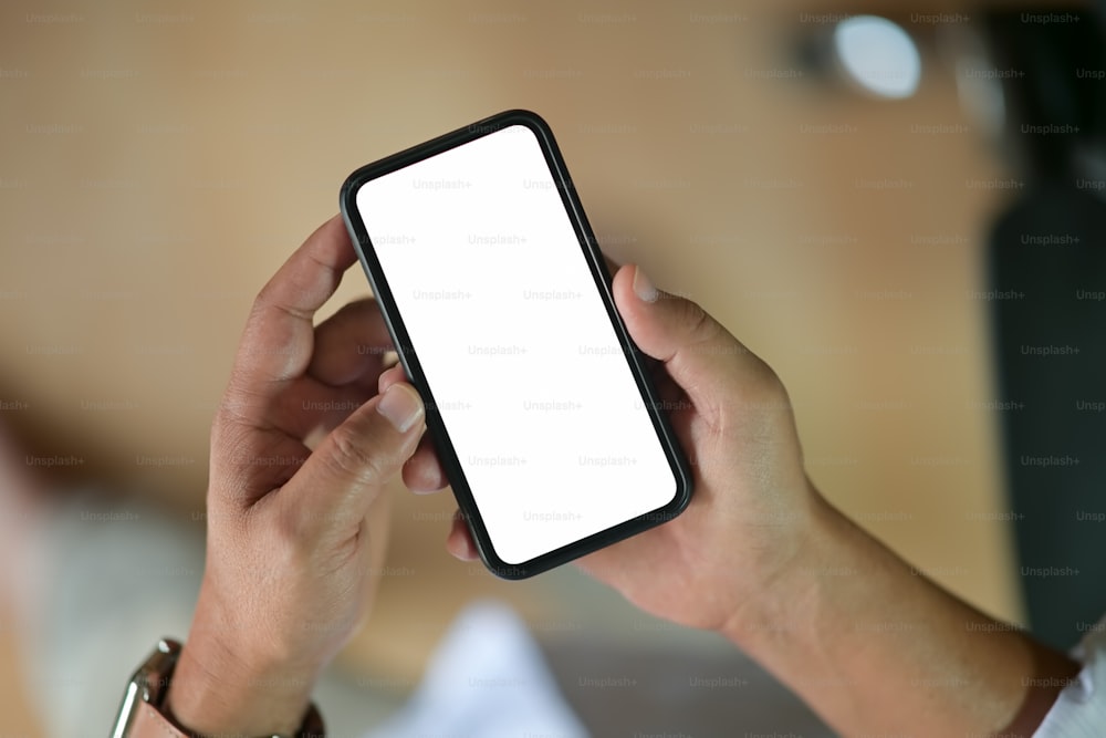 空白の画面のモバイルスマートフォンを保持している男性の手の接写