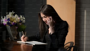 Asian businesswoman calling on mobile phone and taking notes in office