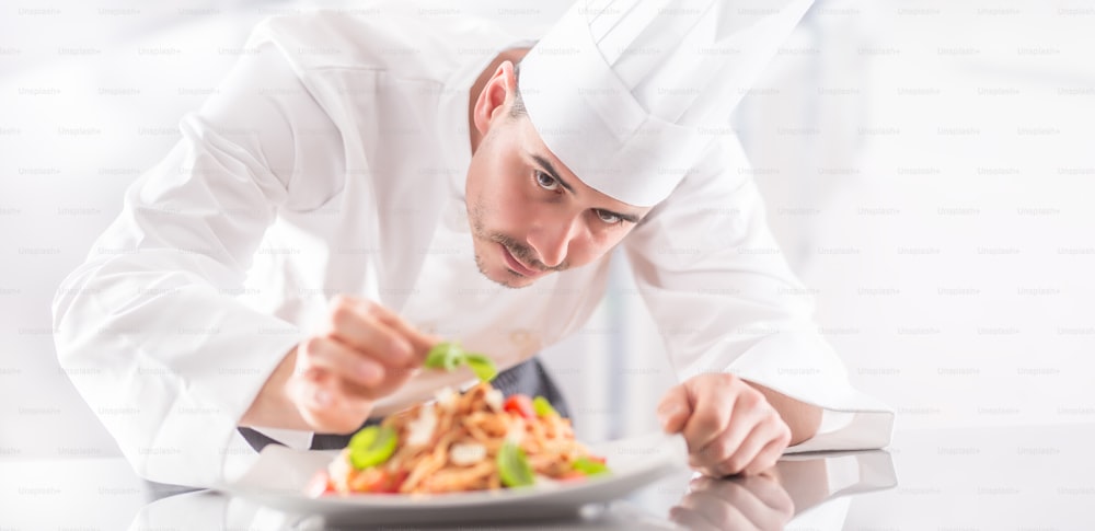 Chef in restaurant kitchen prepares and decorates meal with hands.Cook preparing spaghetti bolognese