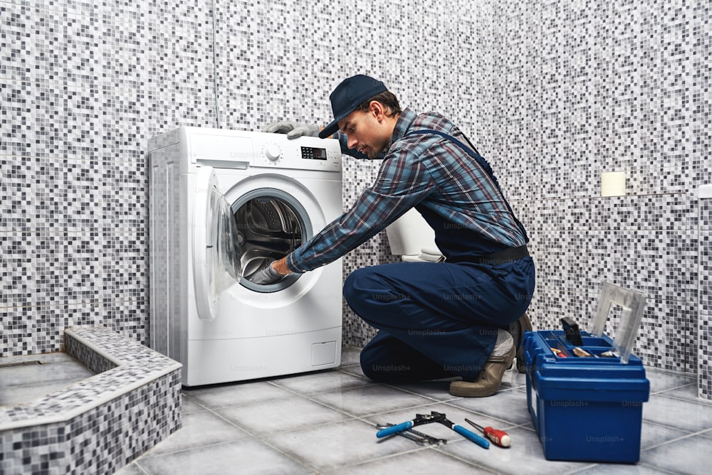 Washing mashine is leaked. Working man plumber repairs a washing machine in laundry