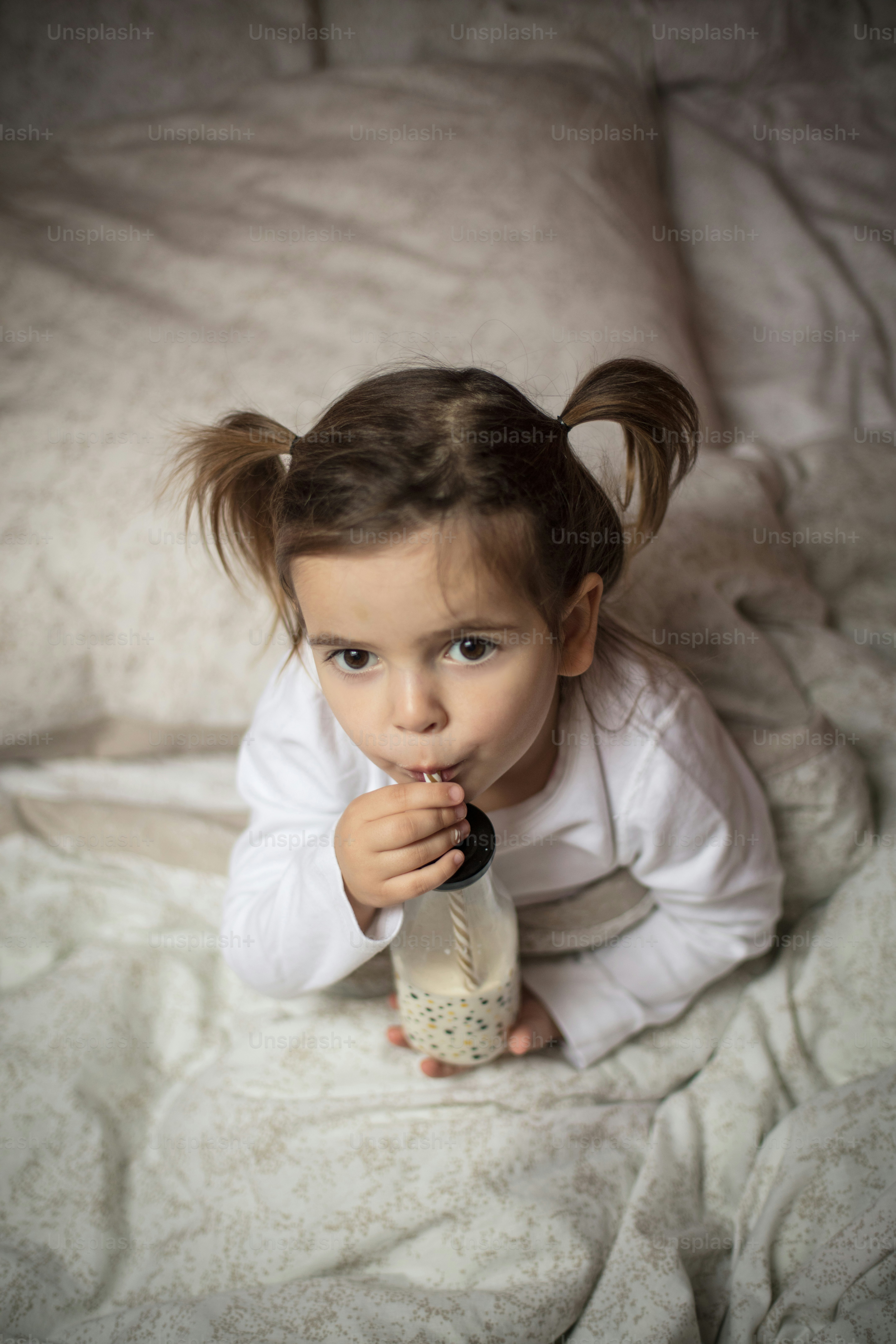 She love to drinking milk. Little girl drinking milk in the bed. Close