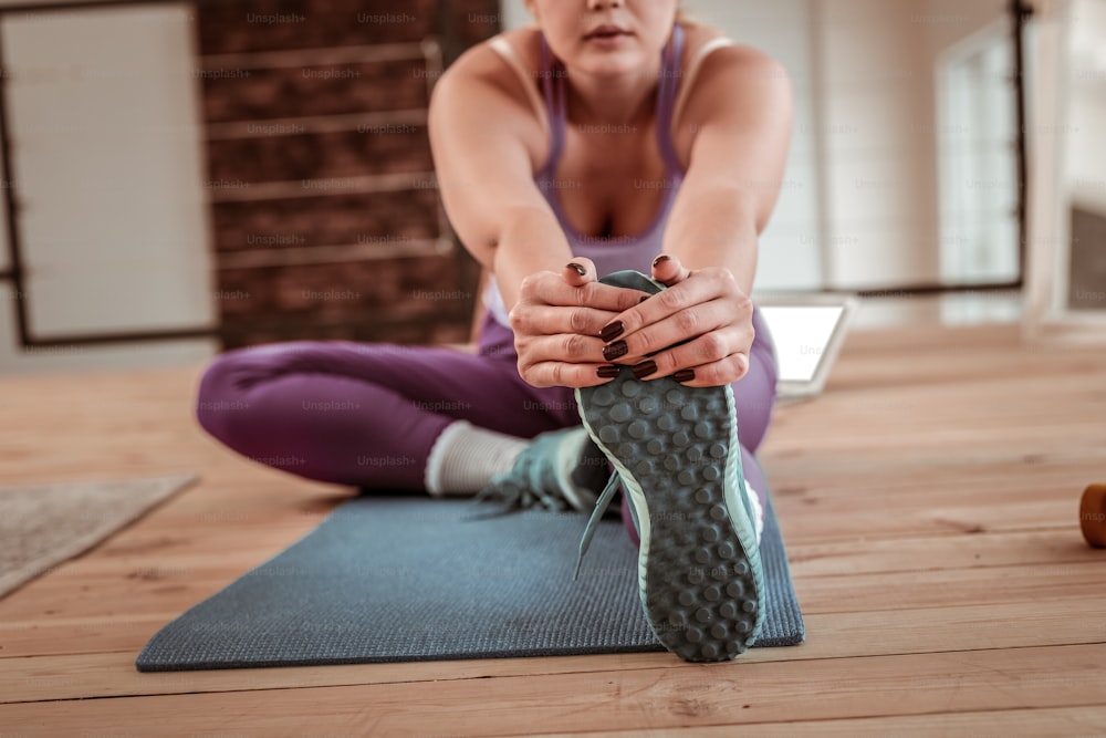Lidiar con el estiramiento. Mujer deportiva de cabello claro mirando a un lado mientras entrena en el piso de madera de su apartamento
