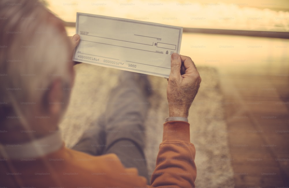Days of age are insured. Senior man holding bank check. Close up. Focus on hand.